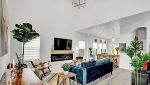 Un salón espacioso con un sofá azul, una mesa de centro de madera y un televisor montado en la pared.