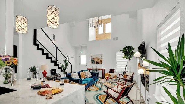 Amplia sala de estar con escalera, un sofá azul, una mesa de comedor con una bandeja de frutas y lámparas modernas.