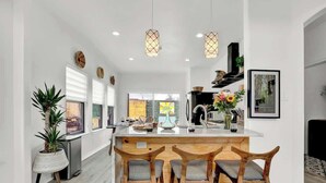 Una cocina moderna con una isla central, sillas de madera, luces colgantes y vistas al exterior.