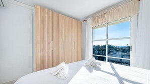A hotel room with a large bed, a wooden wardrobe, and a window with a city view. - Sea Views 1 Bed Apt Colinas Del Faro (El Faro)