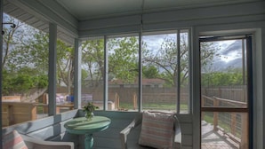 A covered patio with a table and chairs, large windows, and a view of the backyard. - Gorgeous Bluebonnet House With Deck and Fire Pit (Fredericksburg)