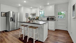 A modern kitchen with white cabinets, stainless steel appliances, and a wooden island with stools. - Gorgeous Bluebonnet House With Deck and Fire Pit (Fredericksburg)
