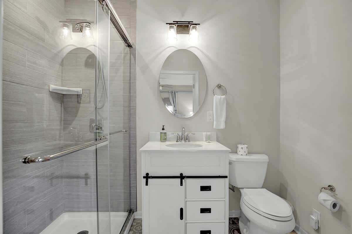 Un baño moderno con cabina de ducha de vidrio, un lavabo blanco con espejo y un inodoro con toallero.