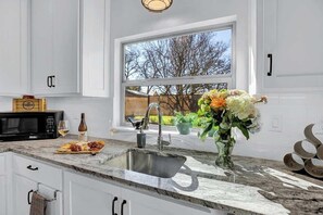 Une cuisine moderne avec une grande fenêtre, un évier, un four à micro-ondes et un verre à vin posé sur le plan de travail.