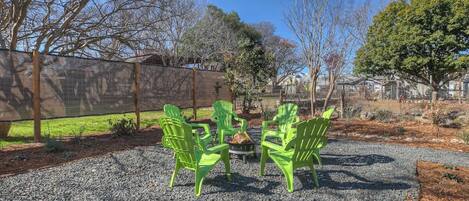 A patio area with four green Adirondack chairs arranged around a small fire pit.