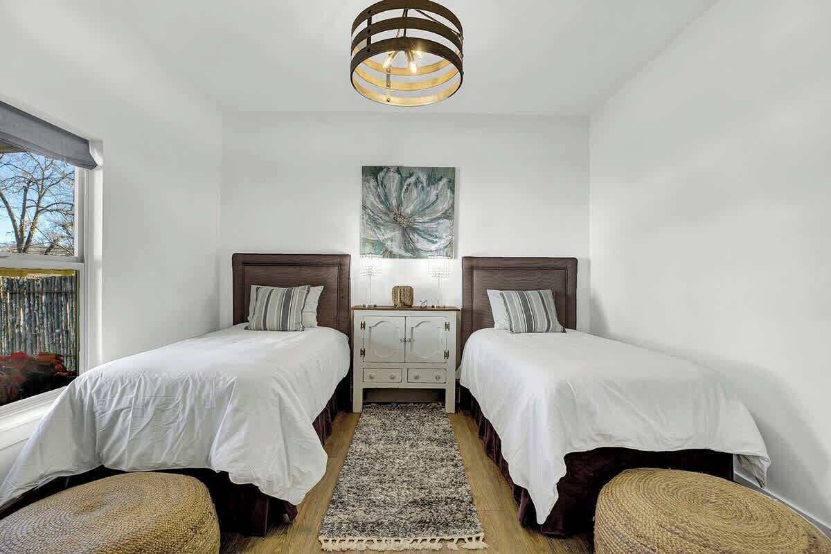 A bedroom with two beds, a wooden nightstand, a large abstract painting, and a window with a view of trees.