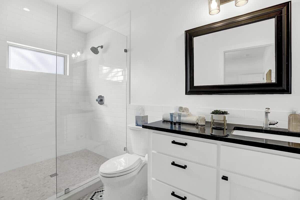 A modern bathroom with a glass shower enclosure, a white toilet, and a vanity with a black countertop.