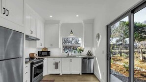 Una cocina moderna con armarios blancos, electrodomésticos de acero inoxidable y un amplio ventanal con vistas al exterior.