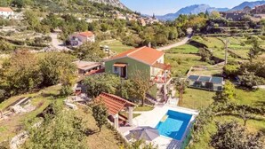 A villa with a swimming pool, surrounded by lush greenery and mountains in the background. - Apartment Dawn with playground and pool (Ostrvica- Omiš)