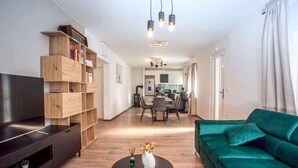 A modern living room with a TV, wooden shelving, a green sofa, and a dining area in the background. - Apartment Dawn with playground and pool (Ostrvica- Omiš)