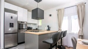 A modern kitchen with a central island, stainless steel appliances, and bar stools. - Apartment Dawn with playground and pool (Ostrvica- Omiš)
