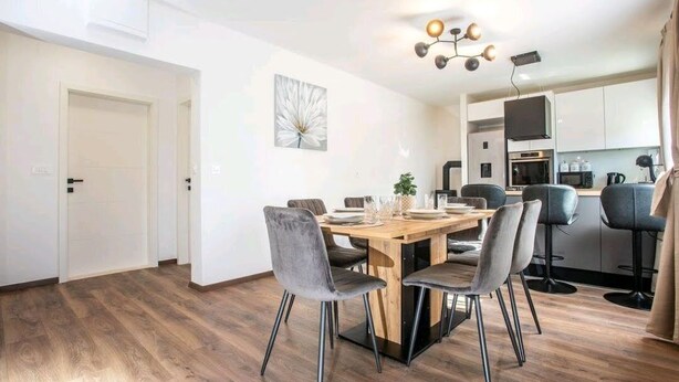 A modern kitchen with white cabinets, a wooden dining table, and grey chairs. - Apartment Dawn with playground and pool (Ostrvica- Omiš)