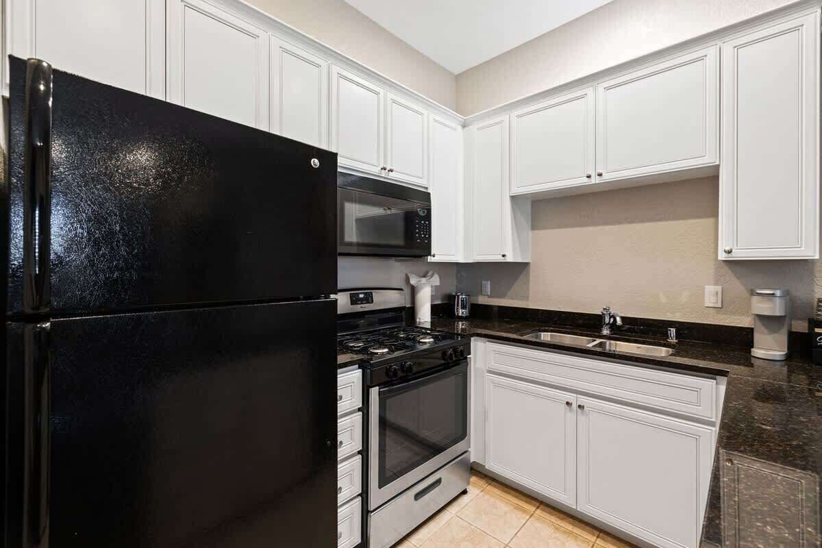 A kitchen with white cabinets, a black refrigerator, a stove, and a sink.