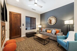 A living room with a sofa, ottoman, coffee table, and a television.