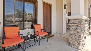 A patio with two orange chairs, a small table, and a stone fireplace.