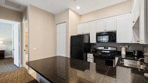 A modern kitchen with white cabinets, a black refrigerator, a microwave, and a stainless steel sink.