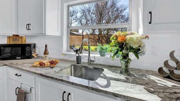 A modern kitchen with a large window, a sink, a microwave, and a wine glass on the counter.
