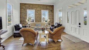 A spacious living room with a wooden accent wall, two large windows, a fireplace, and a white door.