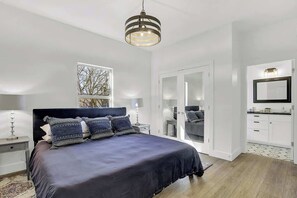 Een moderne slaapkamer met een groot bed, nachtkastjes, een spiegel en een garderobe.