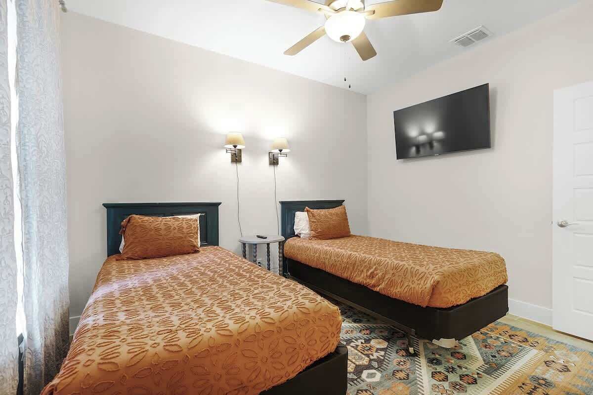 Habitación de hotel con dos camas, ventilador de techo, televisión y alfombra estampada.