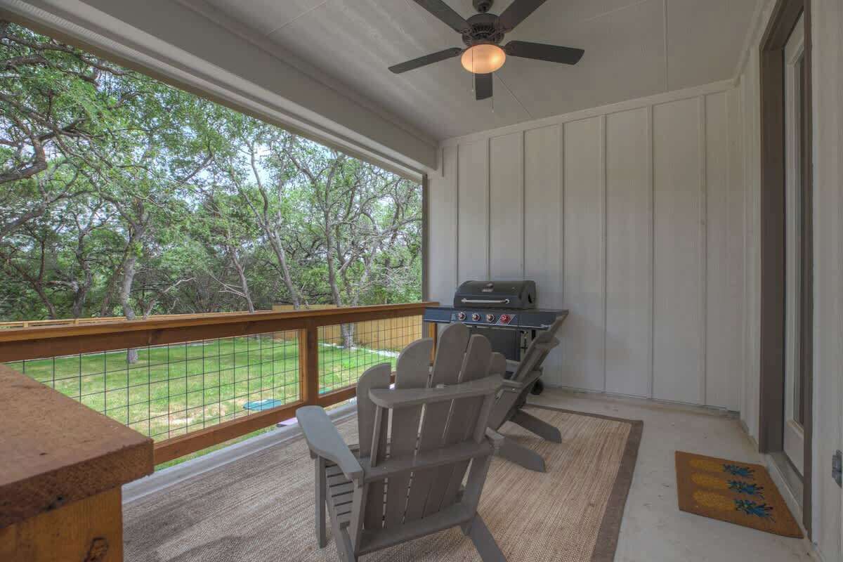 A covered outdoor area with a grill, chairs, and a view of trees.