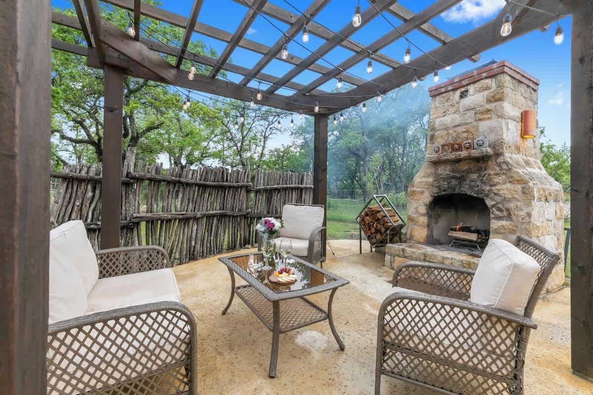 An outdoor patio with wicker furniture, a stone fireplace, and a pergola with string lights.