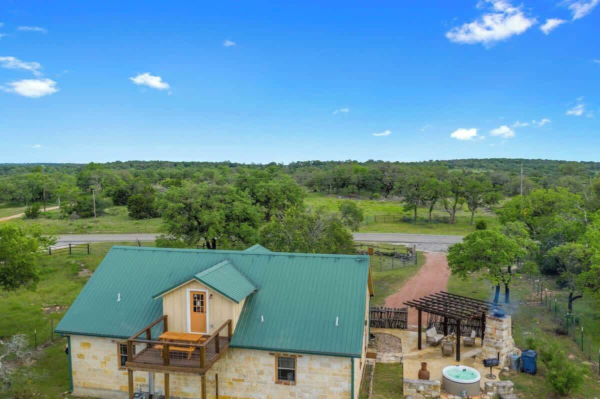 A rustic stone building with a green roof, a patio with outdoor seating, and a scenic view of a forested area.