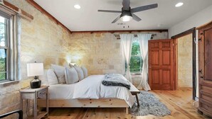 Une chambre avec un mur en pierre, un lit en bois, un ventilateur de plafond et une vue sur l’extérieur.