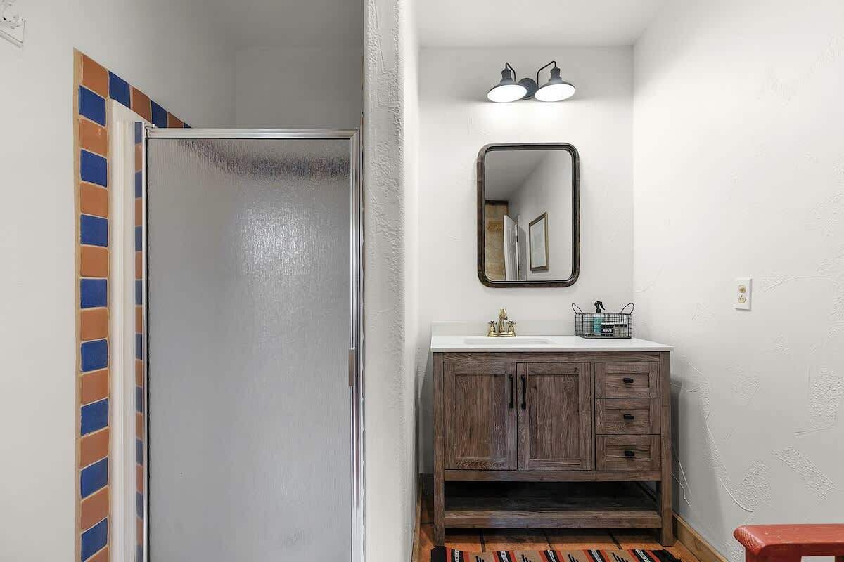 A bathroom with a shower, a sink with a mirror, and a wooden vanity.