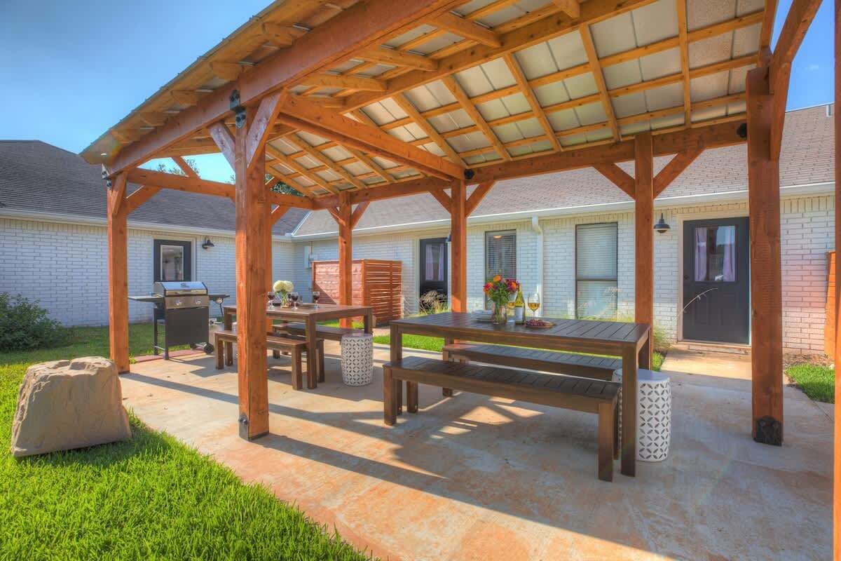Une terrasse extérieure dotée d’une pergola en bois, d’un barbecue et d’une table à manger avec des bancs.