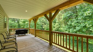 Une terrasse couverte avec des rampes en bois, un barbecue et plusieurs chaises.
