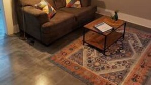 Una sala de estar con un sofá marrón, una mesa de centro, un tapete estampado y una lámpara de pie.