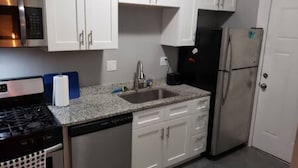 Cocina con armarios blancos, refrigerador de acero inoxidable, microondas y lavavajillas.