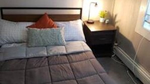 Un dormitorio con cama, almohadas, una mesita de noche con lámpara y un cuadro en la pared.