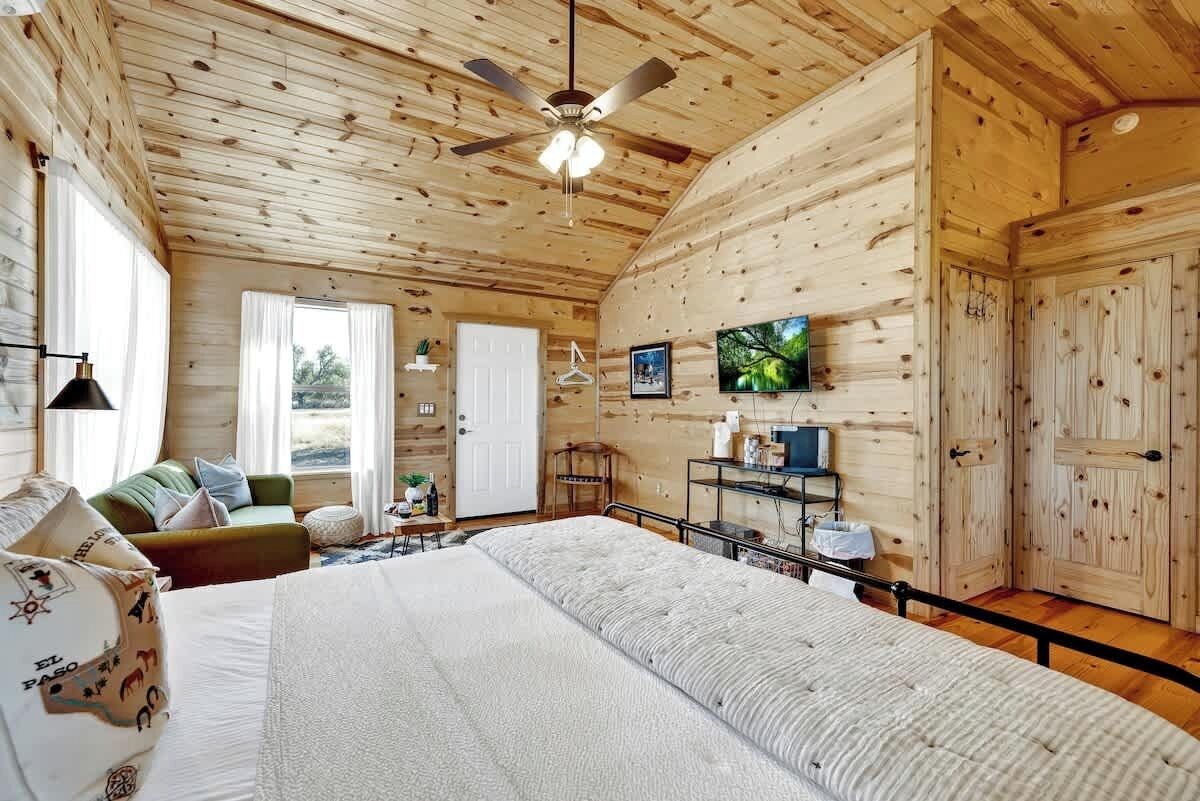 A wooden cabin interior with a bed, a sofa, a television, and a ceiling fan.