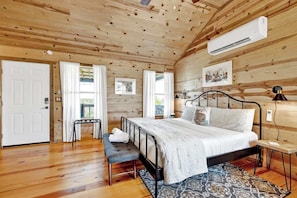A wooden-paneled bedroom with a bed, bench, and artwork. - Rocky Ridge Cedar Cabin With Hot Tub & Amazing Views (Fredericksburg)