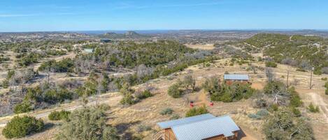 A remote cabin with a metal roof, surrounded by dry grassland and sparse trees.