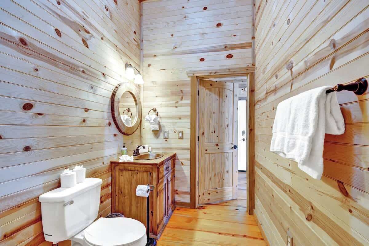 A wooden cabin bathroom with a toilet, sink, and mirror.
