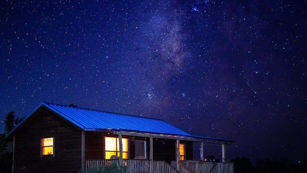 A rustic cabin with a porch, under a starry night sky.