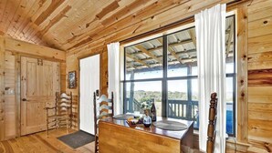 A wooden interior with a dining table, chairs, and a large window offering a view.