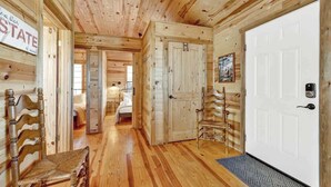 A wooden cabin interior with a hallway leading to a bedroom, a white door, and a chair.