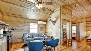 A log cabin interior with a living area featuring a gray sofa, blue chairs, and a wooden ceiling fan.