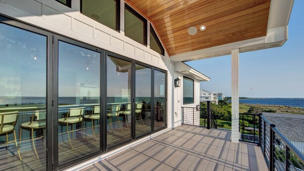 A covered outdoor seating area with glass walls, a wooden deck, and a view of the sea. - 6BR - 6.5 Bath - Sleeps 14-Amazing Sunsets, Creating Lifelong Memories Together  (Salvo)