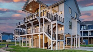 A multi-story waterfront house with balconies, large windows, and a covered outdoor area. - 6BR - 6.5 Bath - Sleeps 14-Amazing Sunsets, Creating Lifelong Memories Together  (Salvo)