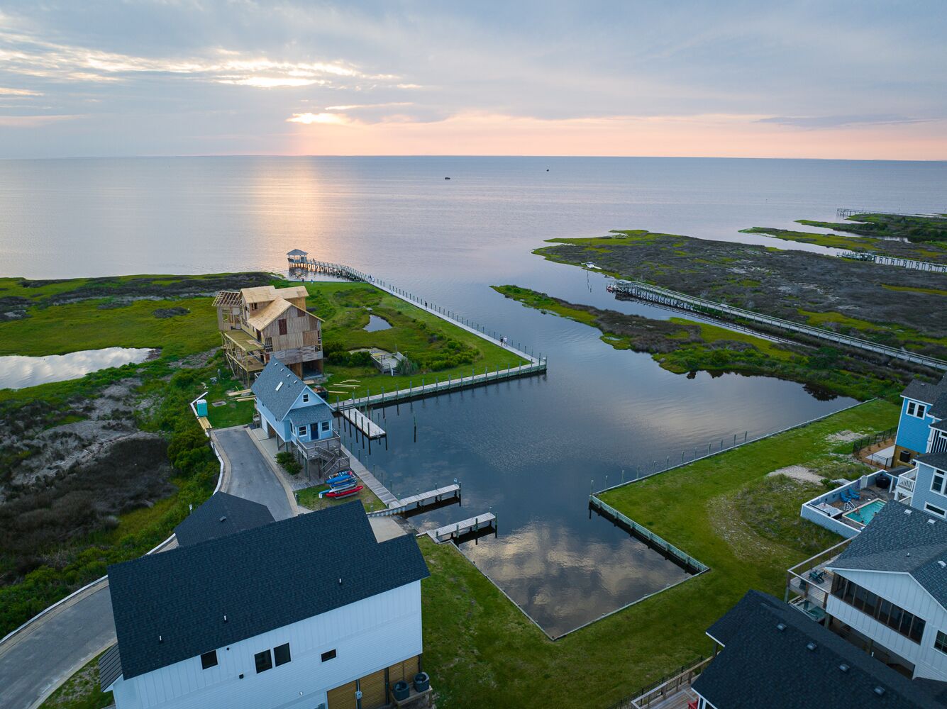 An aerial view of a coastal area with a dock, a small building, and a bridge connecting to an island.