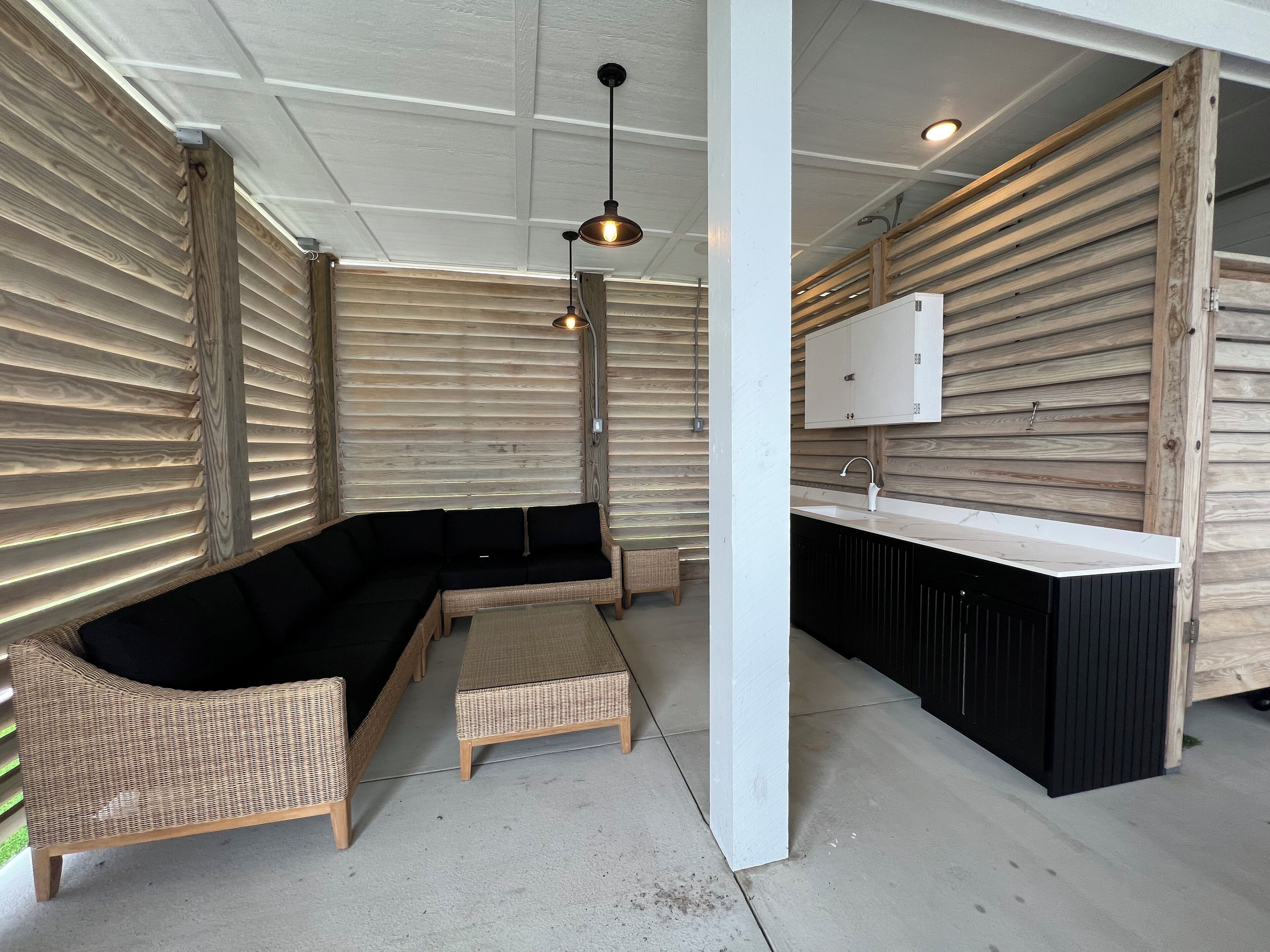 A modern outdoor seating area with a black sectional sofa, wicker chairs, and a small table.