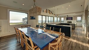 A spacious kitchen with a large island, a dining area with a glass table, and large windows offering ocean views. - 6BR - 6.5 Bath - Sleeps 14-Amazing Sunsets, Creating Lifelong Memories Together  (Salvo)