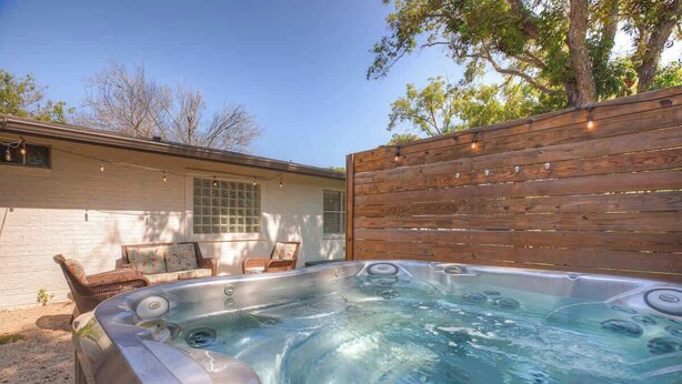 A hot tub in a backyard with a wooden fence, a white house, and a window.