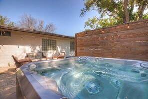 Un jacuzzi en un patio trasero con una valla de madera, una casa blanca y una ventana.