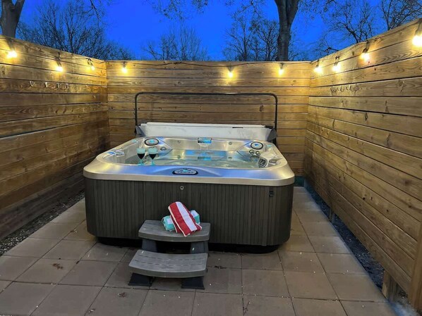 Un jacuzzi con una terraza de madera y un escalón pequeño que lleva hacia él, rodeado por una valla de madera.